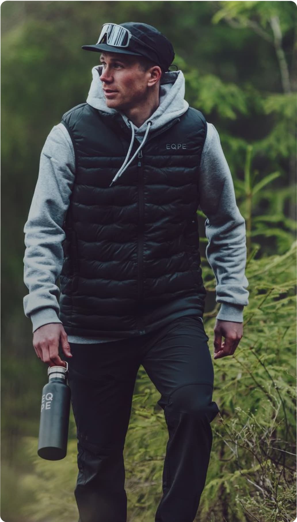 Man in a black outdoor gear walking through a forested area.