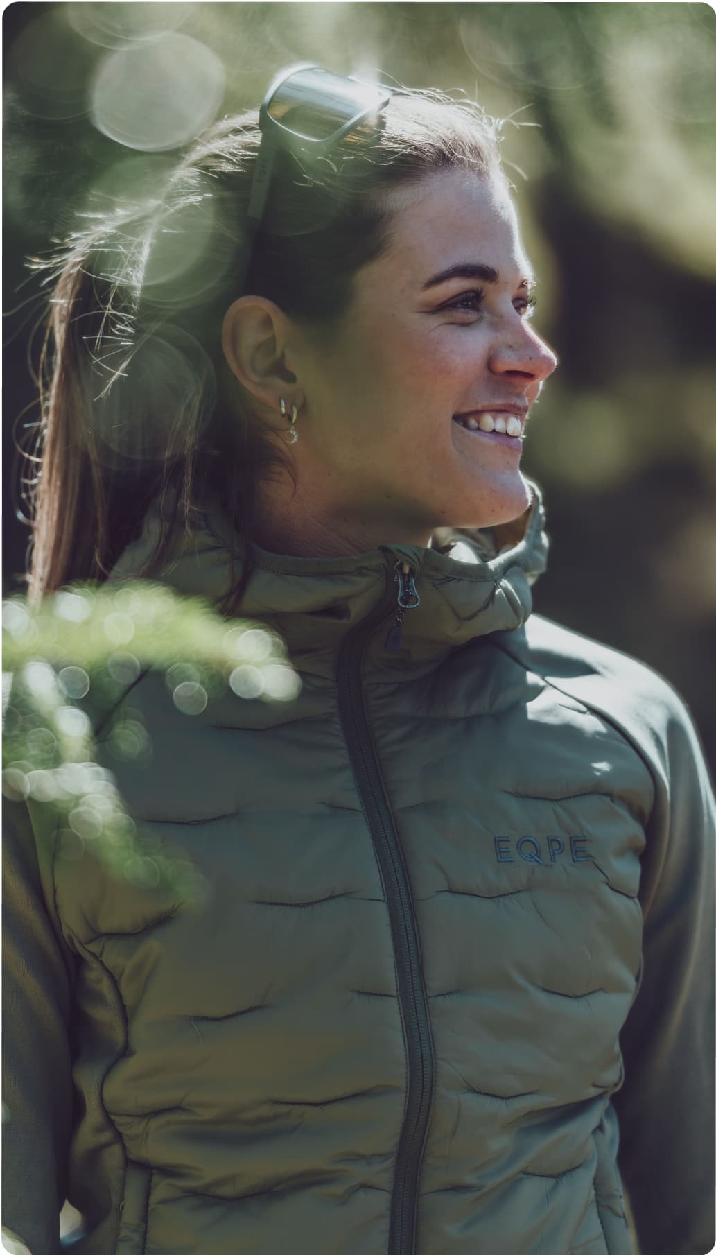 Woman smiling wearing a green mid layer jacket and sunglasses.