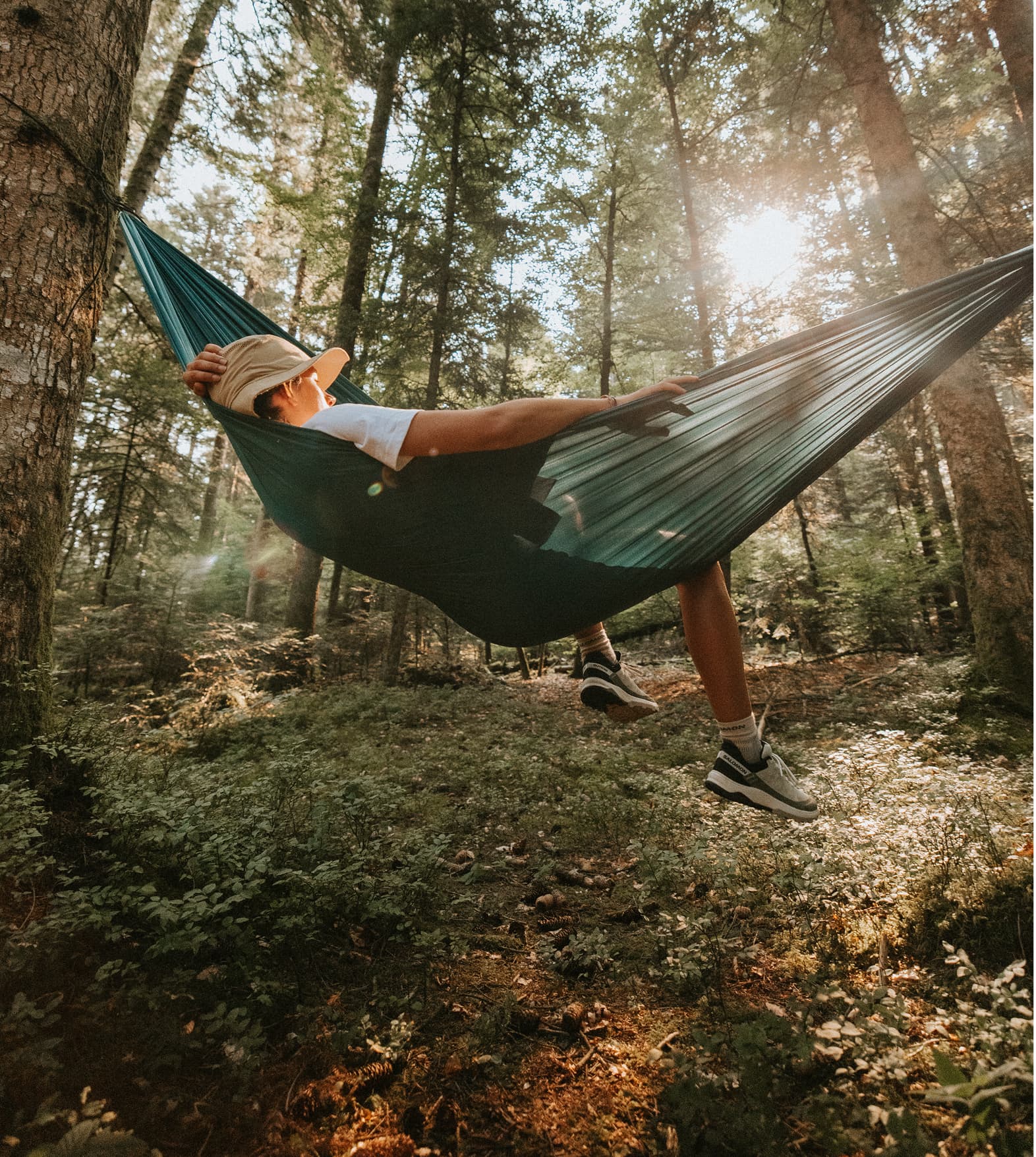 Person relaxing in a green hammock in a forest with sunlight filtering through the trees.