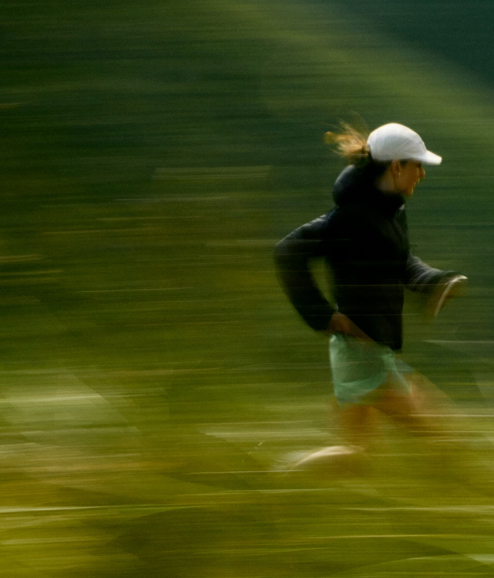Blurred image of a person running through a green, grassy area.