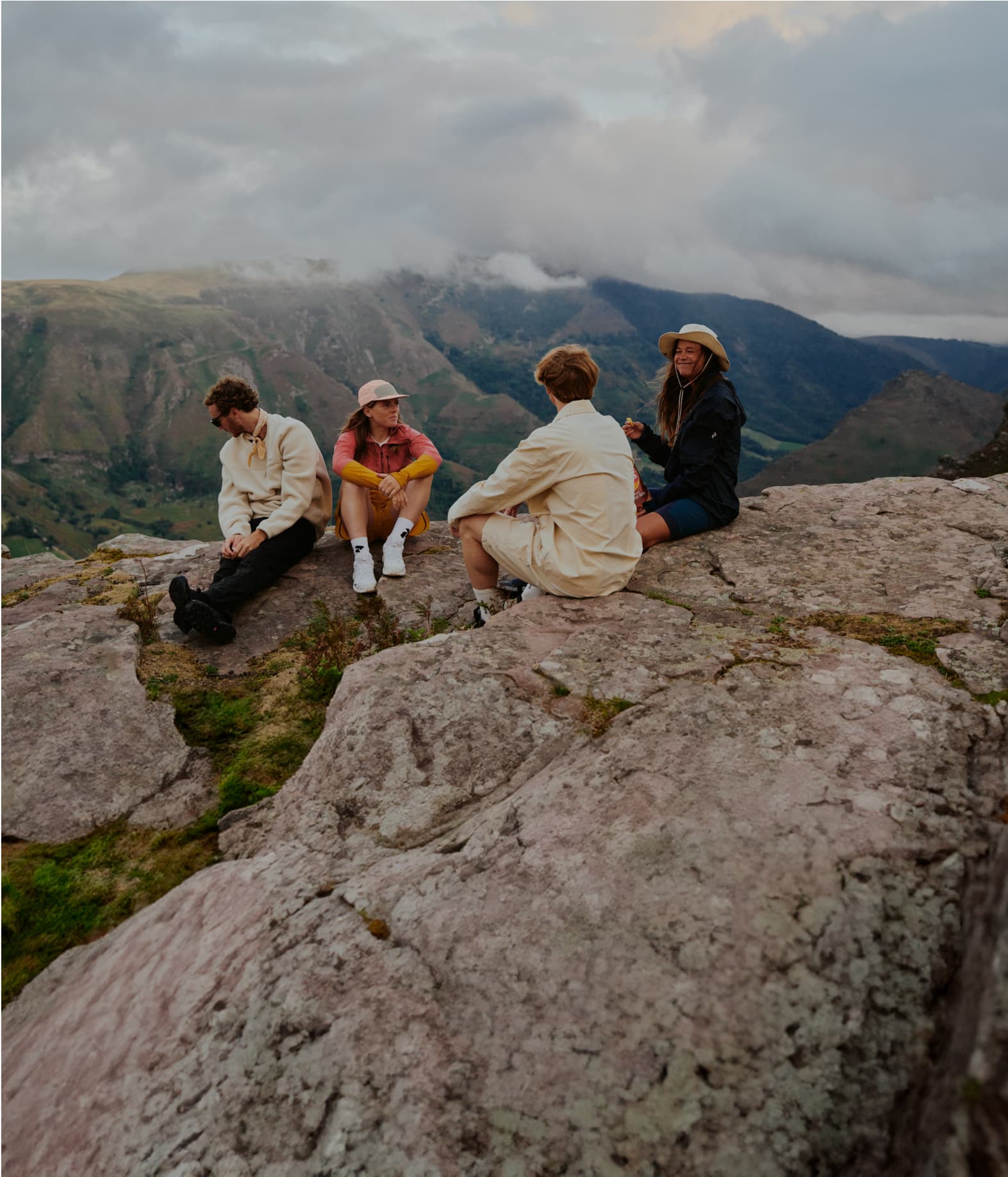 Four people sitting on a rock, dressed in casual outdoor attire.