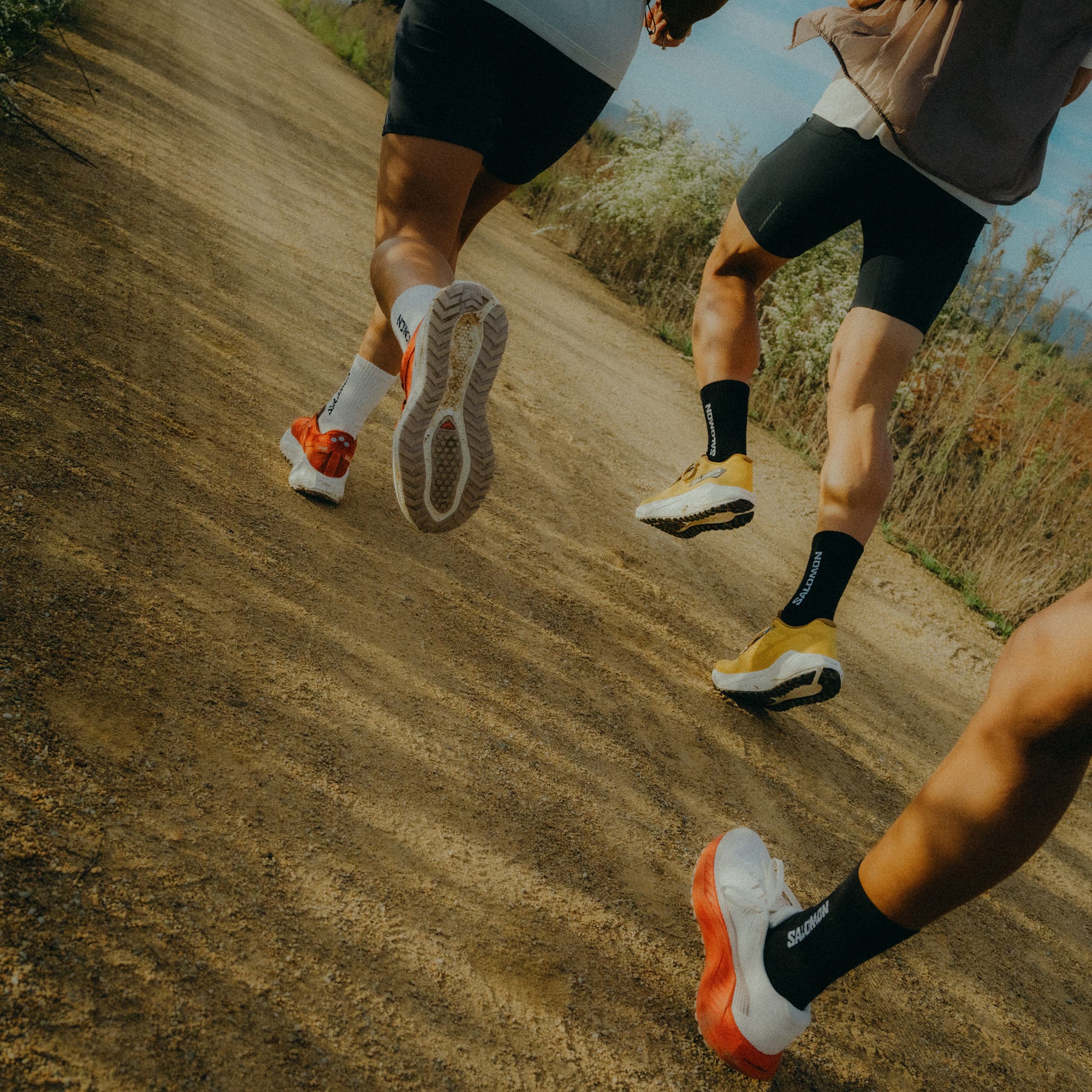Three people running on a dirt path, wearing running shoes.