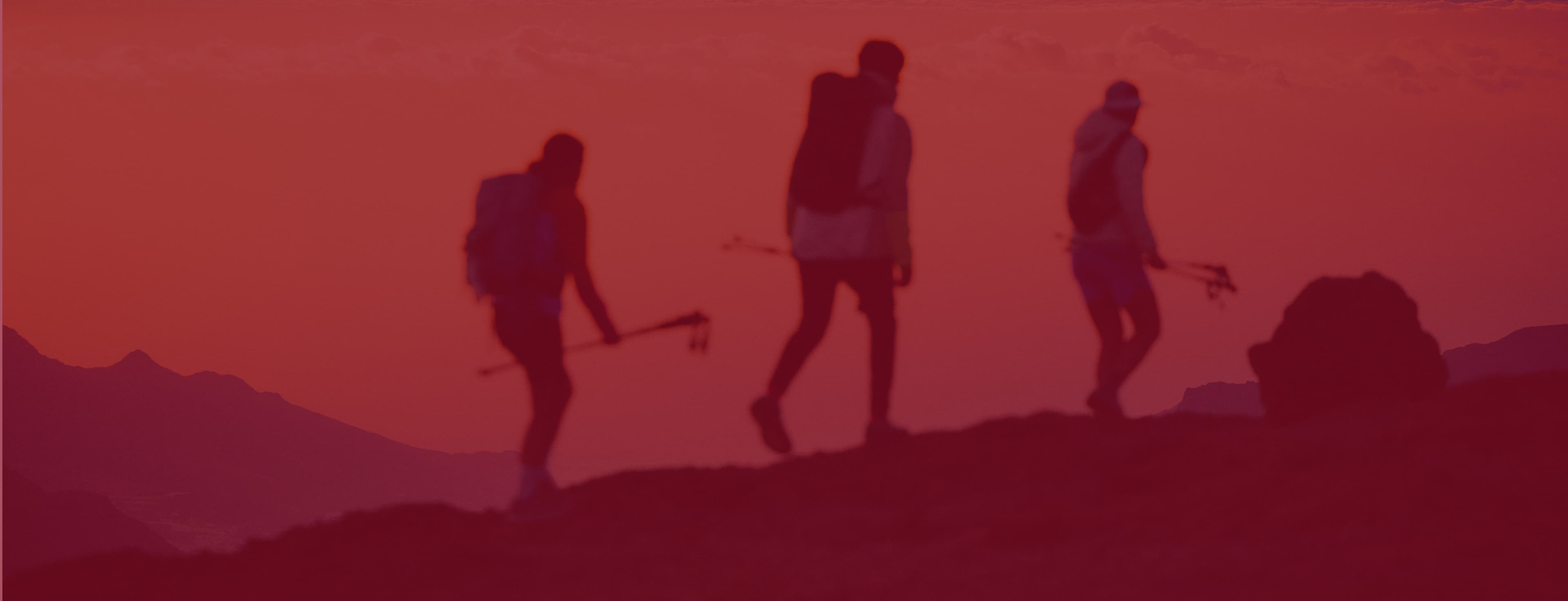 Three silhouettes of hikers with backpacks and trekking poles walking along a mountain ridge.
